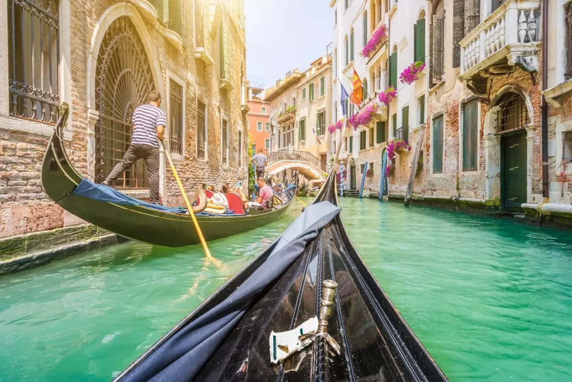 Traditional-gondolas-on-a-narrow-canal-in-Venice-Italy-with-retro-vintage-toned-Instagram-style-grunge-filter-and-lenses-flare-sunlight-effect-on-a-sunny-day-with-blue-skies-in-summer
